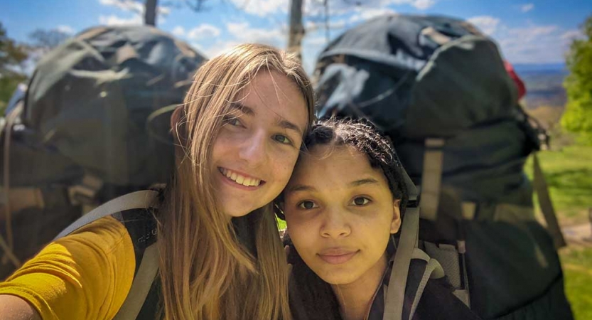 two girls wearing backpacks smile on an outward bound trip near DC